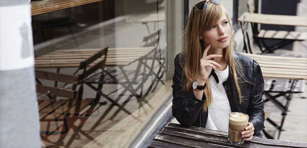 Lady Sitting in Patio Cafe Gracefully Drinking Iced Coffee After Kybella Treatment.